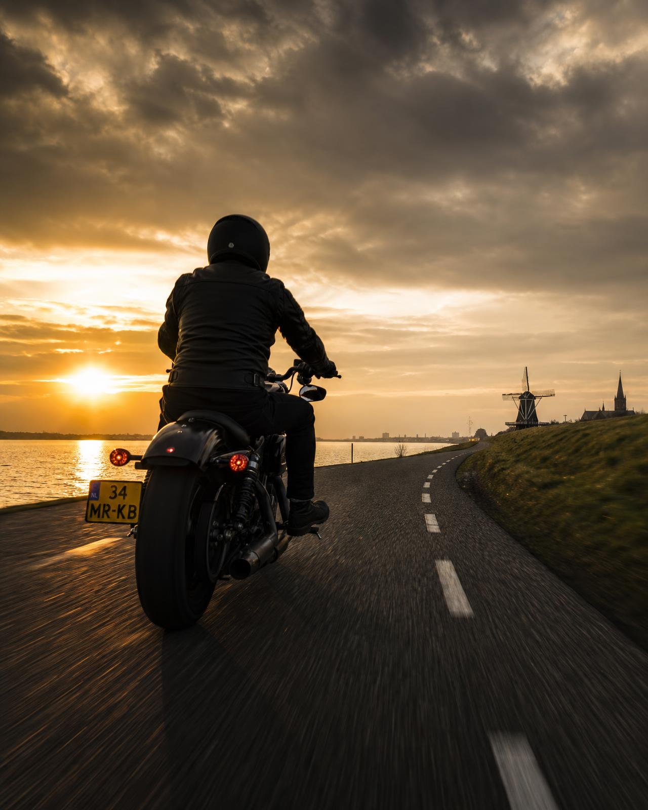 Motorrijder op een dijkweg langs het water bij zonsondergang